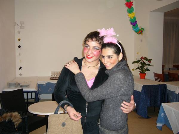 Two women hugging in a festively decorated dining room, one in clown-style makeup