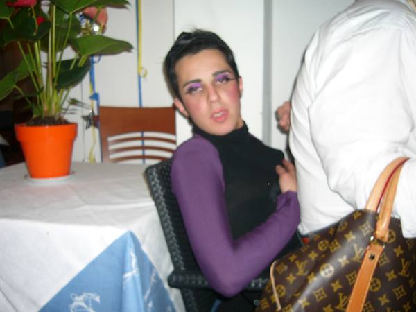 Young woman with purple makeup at a set table, next to a Louis Vuitton bag