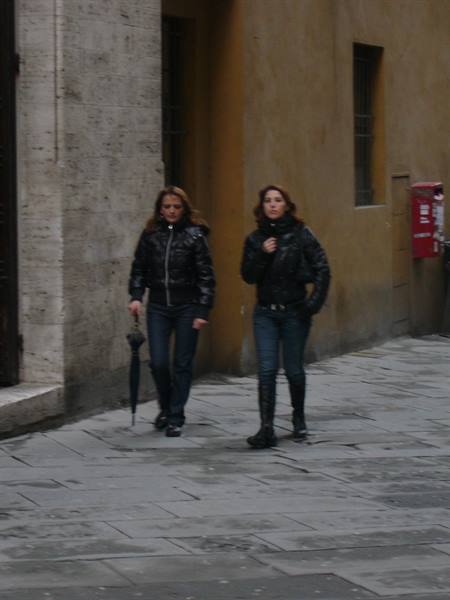 Two women in black jackets walking on stone pavement in Viareggio