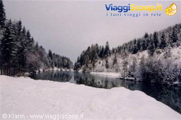 still snow-covered river between white conifers under grey sky