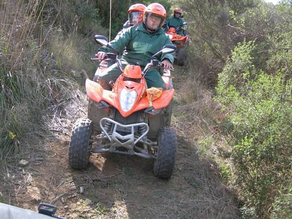 Group on orange quad bikes with red helmets on dirt trail among bushes