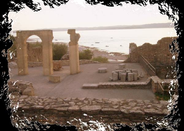Roman ruins with stone arch and columns facing the calm sea