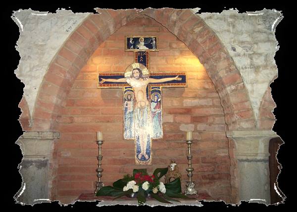 Medieval painted crucifix under brick arch, with candles and flowers on the altar