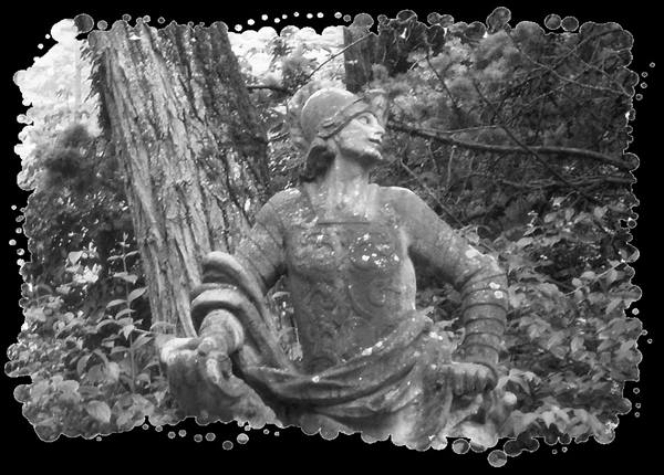 Stone warrior statue with helmet among trees, black and white photo