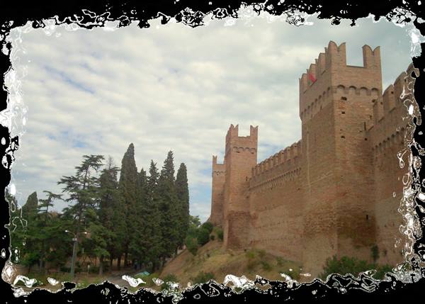 Brick crenellated walls of Gradara castle among cypresses under cloudy sky
