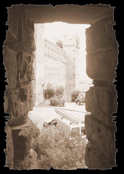 Gradara medieval walls seen through a stone arrow slit, cars below