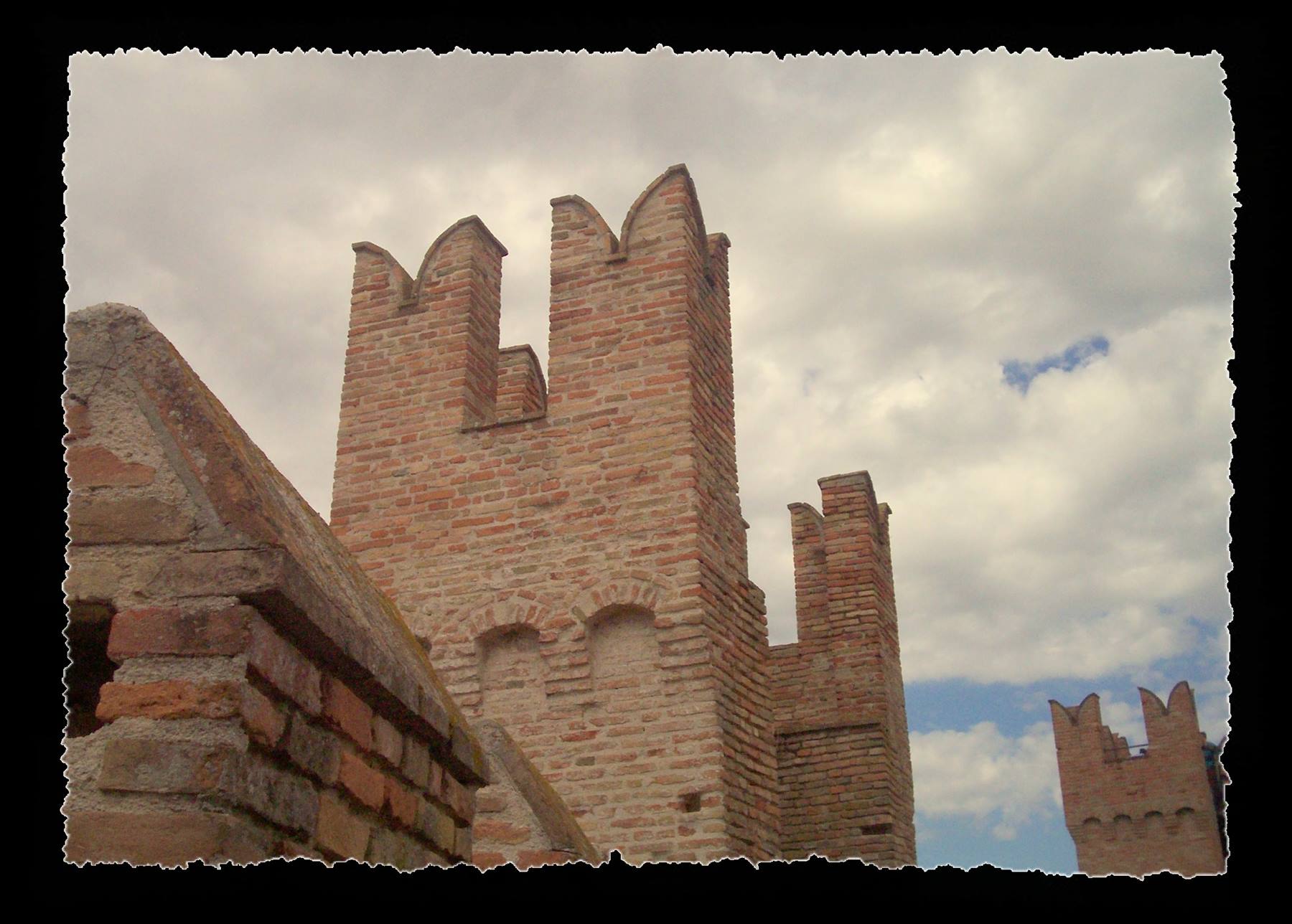 Brick tower with swallowtail merlons, Gradara, against white clouds