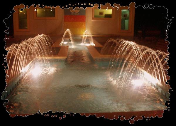 Illuminated fountains at night in a pool, water arcs, lit building windows