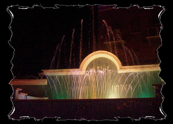 Illuminated fountain at night, rainbow jets in front of white arch