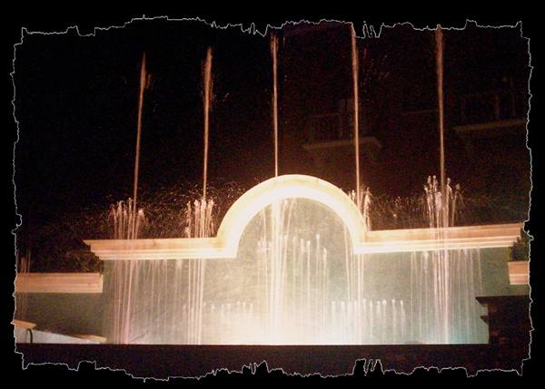 Illuminated fountain at night with water jets before an arch
