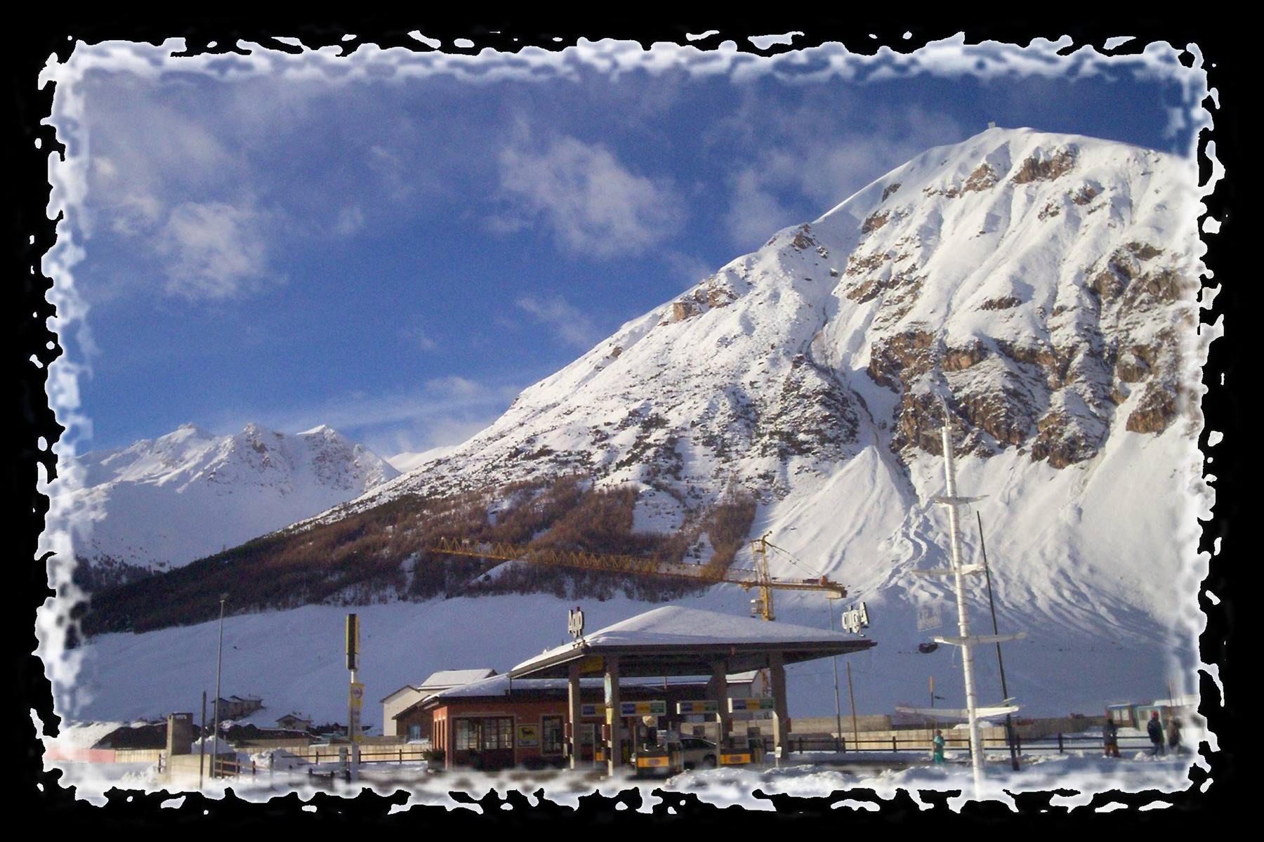 Snow-covered gas station and yellow crane beneath a huge snowy mountain
