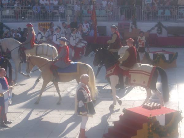 Riders in medieval costumes parade on horses in a crowded square