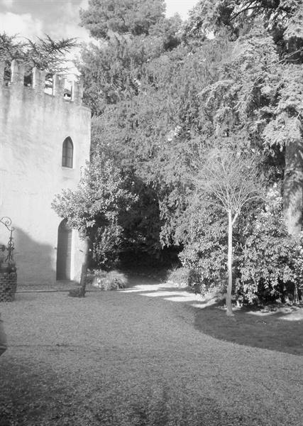 crenellated stone tower with arched window, gravel path among trees, black and white