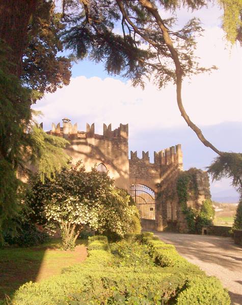Stone crenellated walls with iron gate among trees and garden
