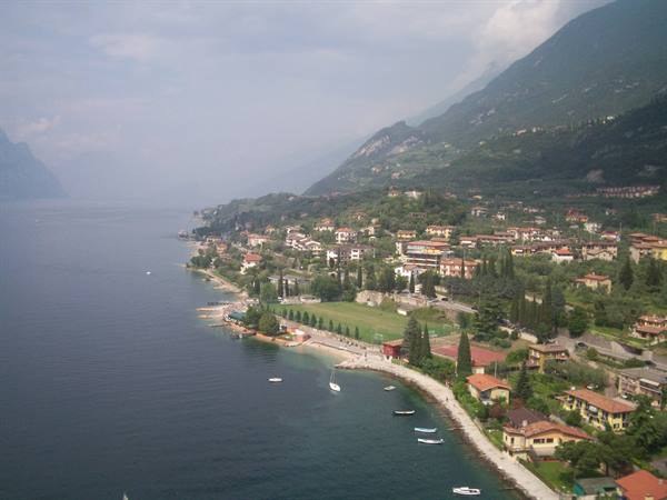 Red-roofed village on Lake Garda shore, small boats and green mountains