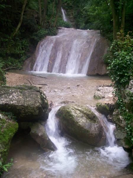 Waterfall flowing over limestone rocks among mossy boulders and green trees