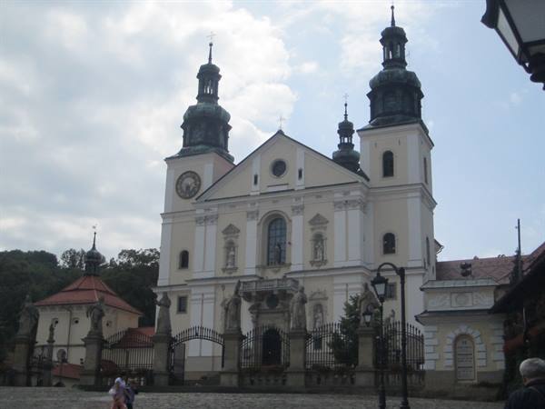 Baroque basilica with two green towers and iron gate, people walking
