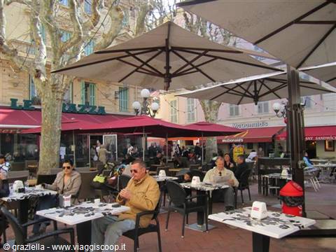 Café terrace with large umbrellas, people seated at tables among plane trees