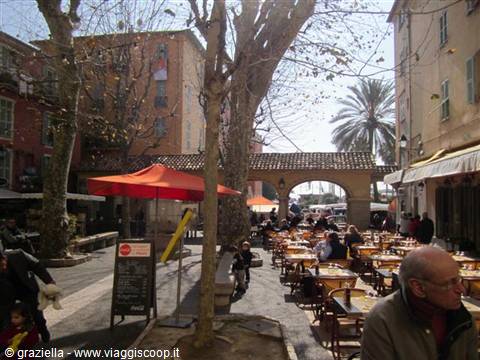 Bormes-les-Mimosas: outdoor café tables under stone arches, red umbrella, winter sun
