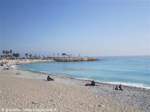 Pebble beach with sunbathers and rocky breakwater on turquoise sea