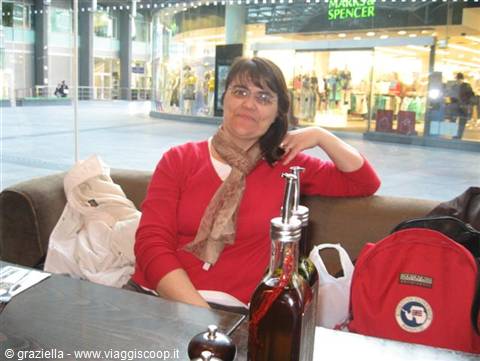 Woman in red sweater seated at café table with oil bottles in front of Marks & Spencer