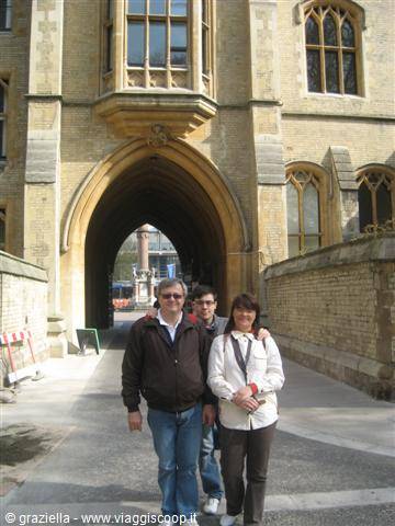 Smiling tourists under the gothic stone archway of a university college