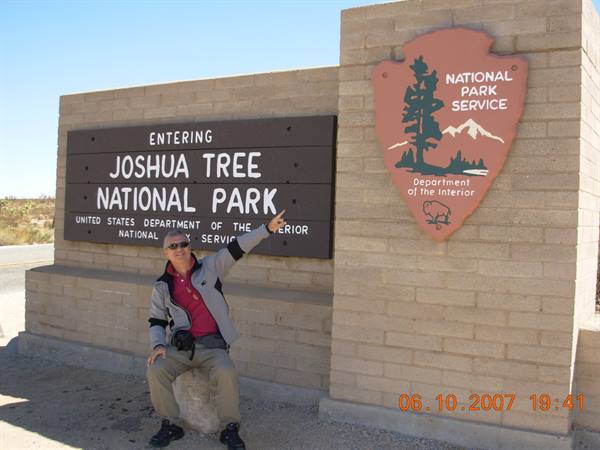 Tourist sitting and pointing at the Joshua Tree National Park entrance sign