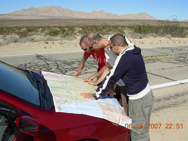 Three friends check a map on the car hood in the desert