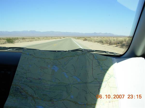 Paper map on dashboard before a desert road, distant mountains, bright light
