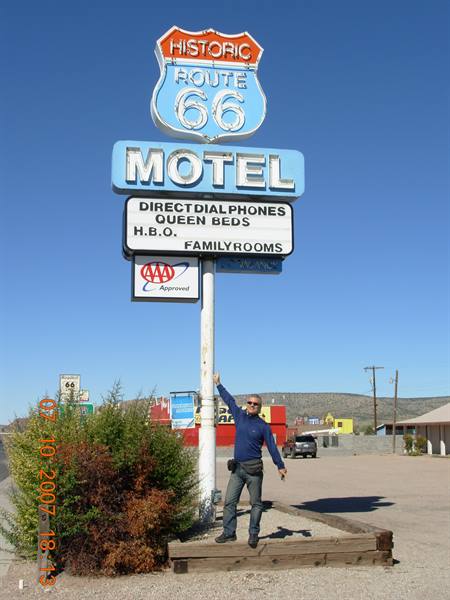 Man pointing at the historic Route 66 motel sign, enamel metal, blue sky, Seligman
