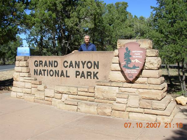 Man beside the Grand Canyon National Park stone sign among trees