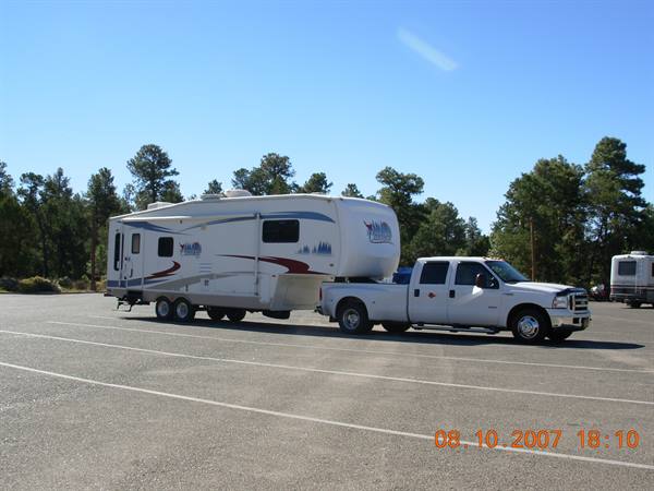 White pickup truck towing a fifth-wheel trailer in a pine tree parking lot