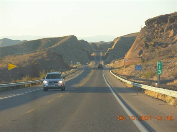 Cars driving a desert highway between rocky hills in morning light