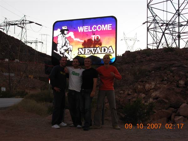 Four friends pose in front of the Welcome to Nevada sign near power lines