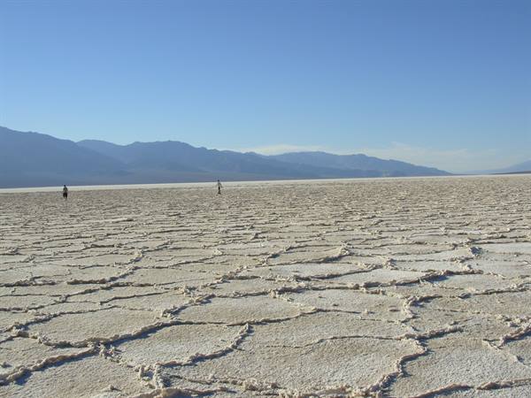 Tourists walking on cracked salt at Badwater Basin, blue mountains behind