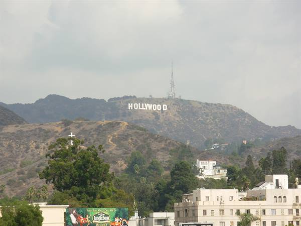 The Hollywood sign on the dry hill, white buildings and trees under a cloudy sky