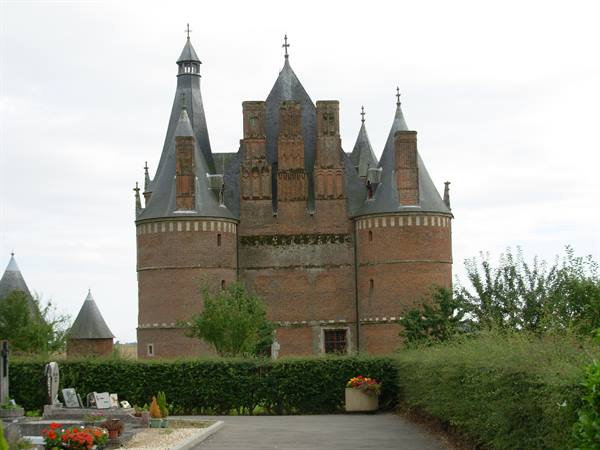 Brick castle with slate conical towers, flowered cemetery in front