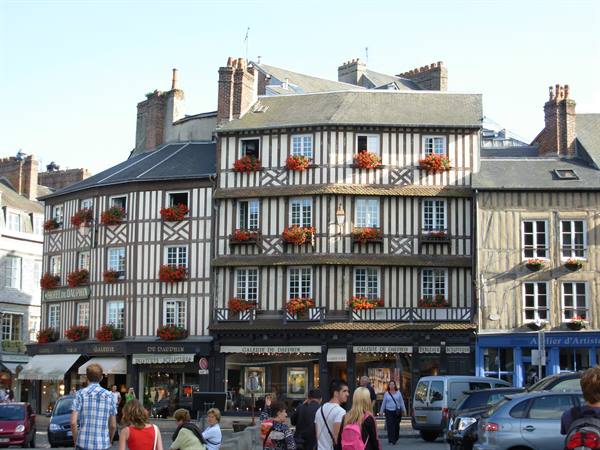 Half-timbered houses with flower boxes, pedestrians and cars below, likely Rouen
