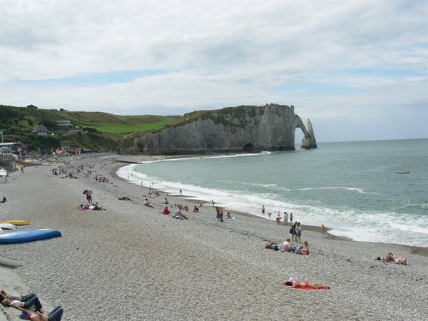 Étretat pebble beach, sunbathers beneath the white cliff with natural arch