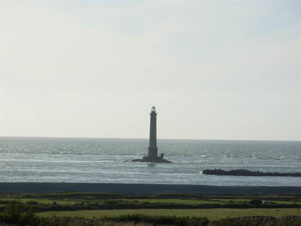 Stone lighthouse on a rock in choppy sea, green field in foreground