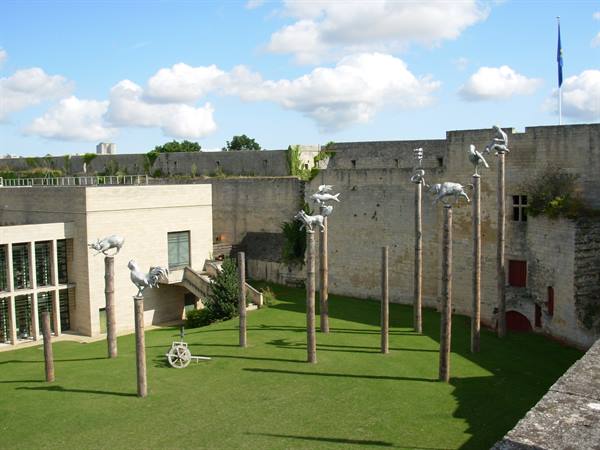 Animal sculptures on wooden poles in the grassy courtyard of Caen castle