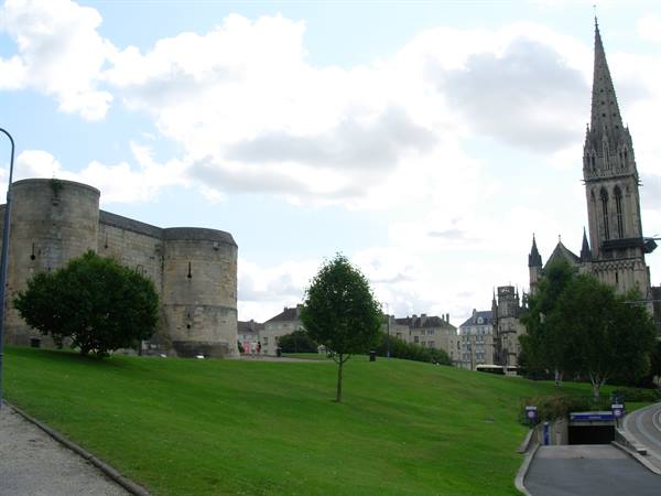 Caen castle stone towers on green lawn, Saint-Pierre church spire, cloudy sky
