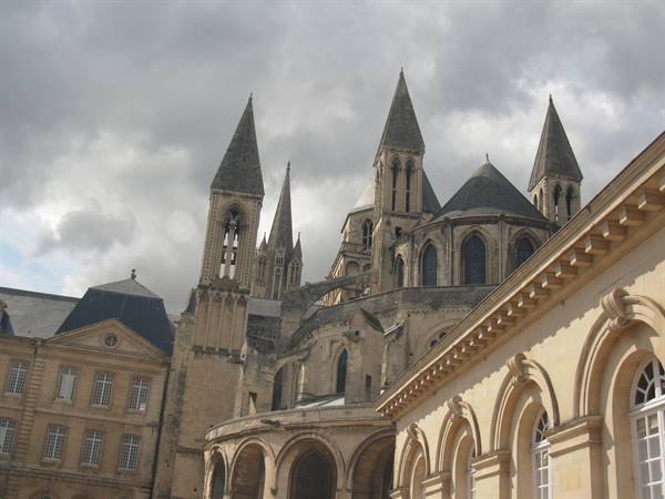 Gothic spires of Caen abbey under cloudy sky, pale stone