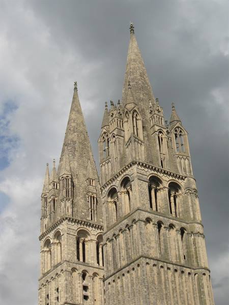 Gothic stone spires of Bayeux cathedral against grey clouds