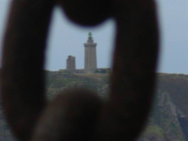 Lighthouse seen through a rusty chain link, cliffs below