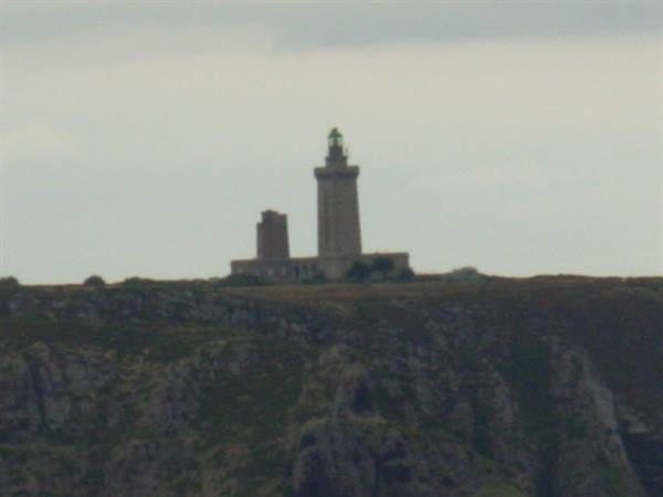 Cap Fréhel lighthouse standing on dark rocky cliffs under grey sky