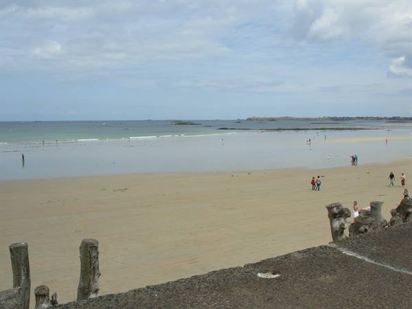 Sandy beach with strolling bathers, wooden posts in the foreground