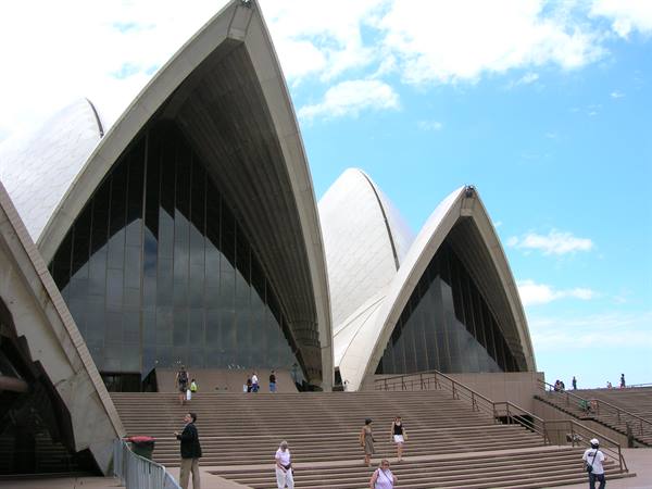Tourists climb the steps of the Sydney Opera House under a blue sky