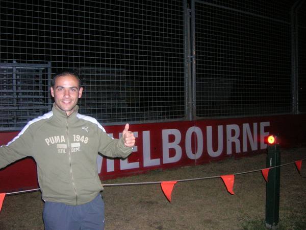 Man in Puma sweatshirt smiles and gives thumbs up before Melbourne sign