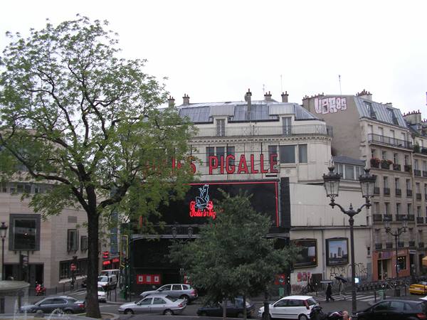 Red neon Moulin Rouge sign in Pigalle, Paris, among trees and traffic